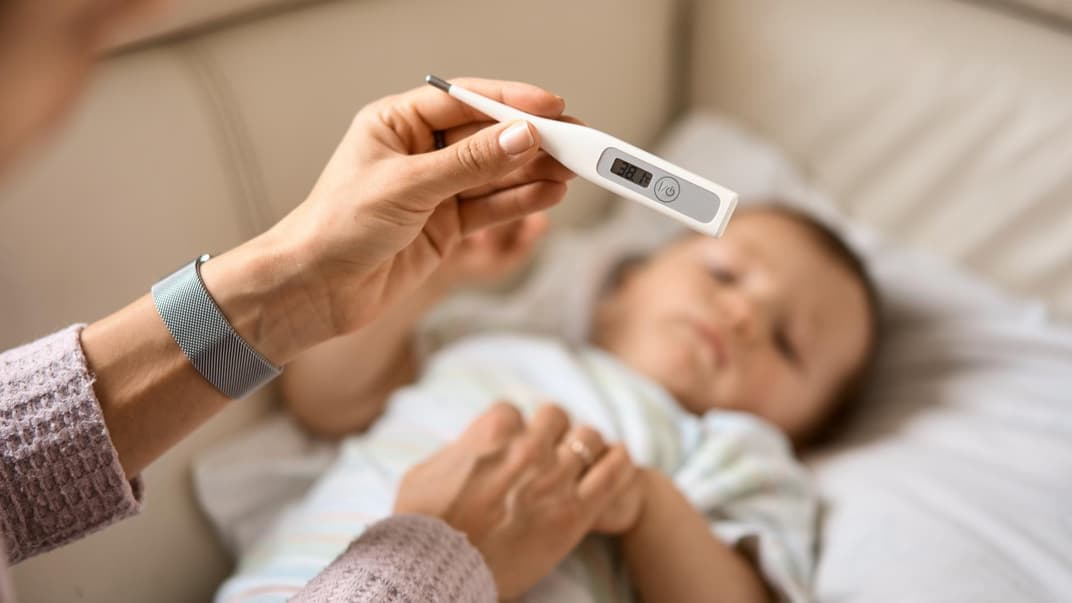 Fiebersaft oder Zäpfchen, was wirkt schneller? Eine Mutter hält das Fieberthermometer über ihrem Baby.