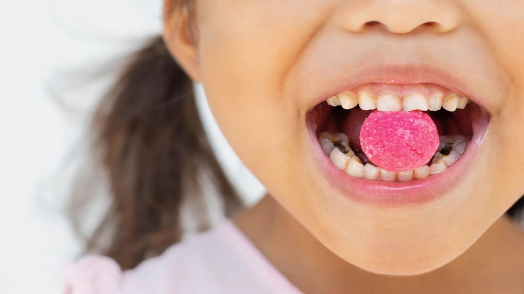 Keine Überraschung: Süßigkeiten fördern Karies. Ein Mädchen mit Bonbon zwischen den Zähnen.