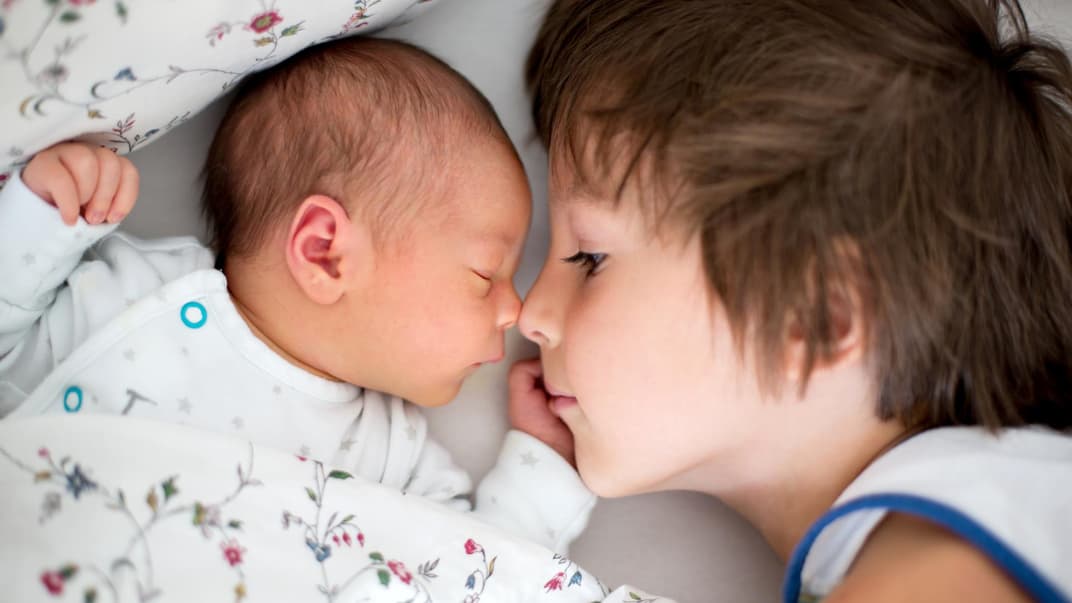 Geschwisterkonstellationen haben einen Einfluss auf unsere Entwicklung. Großer Bruder liegt neben Baby im Bett.