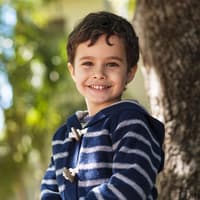 Spanische Jungennamen haben oft besonders schöne Bedeutungen. Ein dunkelhaariger Junge mit blau-weiß gestreiftem Pullover lächelt.