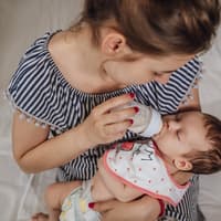 Eine junge Frau gibt ihrem Baby Pre-Milch mit dem Fläschchen Eine junge Frau füttert ihr Baby mit der Flasche