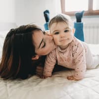 Eine junge Mutter küsst ihre kleine Baby-Tochter auf die Wange. Eine junge Mutter küsst ihre kleine Baby-Tochter auf die Wange.