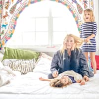 Ausgelaugte Mutter sitzt auf Bett, Kinder ziehen an ihren Haaren und machen Quatsch. Ausgelaugte Mutter sitzt auf Bett, Kinder ziehen an ihren Haaren und machen Quatsch.