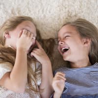 "Alle Kinder Witze" sind oft ganz schön gemein, aber auch sehr lustig. Zwei Mädchen liegen lachend auf dem Boden.