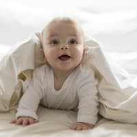 Ein kleiner Baby-Junge guckt frech unter einer weißen Bettdecke hervor. Ein kleiner Baby-Junge guckt frech unter einer weißen Bettdecke hervor.