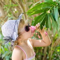 Mädchen mit Hut und Sonnenbrille riecht an einem Blumenstrauch im Garten Mädchen mit Hut und Sonnenbrille riecht an einem Blumenstrauch im Garten