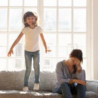 Kind hüpft auf dem Sofa neben erschöpfter Mama. Kind hüpft auf dem Sofa neben erschöpfter Mama.