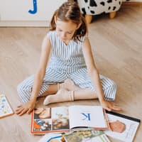 Bilderbücher sind auch in der Grundschule noch angesagt Ein Mädchen liest Bücher auf dem Boden.