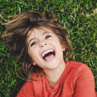 Kinderwitze für jedes Alter. Ein Mädchen, das im Gras liegt und lacht.