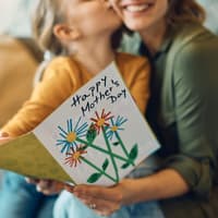 Über eine selbst gestaltete Karte freut sich wohl jede Mama zum Muttertag. Kind küsst Mutter und schenkt ihr eine Karte zum Muttertag.