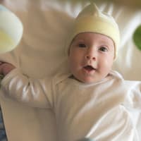 Dein Baby wird von deinem selbst gebastelten Mobile ganz begeistert sein. Baby liegt fröhlich unter einem Mobile.