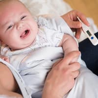 Wenn das Fieber nicht runter geht, machen viele Eltern sich Sorgen um ihr Kind. Eine Mutter misst bei ihrem weinenden Baby mit einem Fieberthermometer die Temperatur.