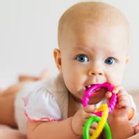 Zahnen kann für Babys mitunter ganz schön unangenehm sein. Gekühlte Schnuller oder Ringe können helfen. Baby liegt auf dem Bauch und kaum am Beißring.