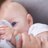 Trinkt das Baby aus der Flasche, kann man die genaue Menge einsehen – beim Trinken an der Brust ist das leider nicht so einfach. Baby mit Schnuffeltuch auf Mamas Arm.