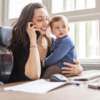 Als Mutter allen Ansprüchen gerecht zu werden, ist nicht immer leicht! Mutter arbeitet mit Kind auf dem Schoß.