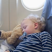 Dank Sitzverlängerung können Kinder im Flugzeug bequem schlafen. Ein kleiner Junge schläft im Flugzeug.