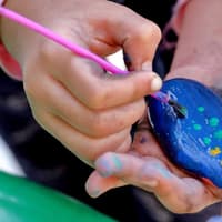 Steine bemalen macht Spaß und fördert die Grob- und Feinmotorik. Kind bemalt einen Stein.