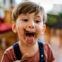Einen Trick gegen ständiges Langeweile-Naschen? Das wünschen sich wohl viele Eltern! Kind streckt mit Schoko-verschmiertem Gesicht die Zunge raus.