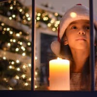 Für viele Kinder ist die Weihnachtszeit etwas ganz Besonderes. Ein Mädchen schaut aus einem weihnachtlichen Fenster.