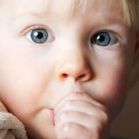 Über das Für und Wider von Daumenlutschen streiten sich die Experten. Kleines Kind nuckelt mit großen Augen am Daumen.