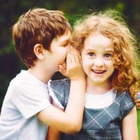 Kinder lieben es, Geheimnisse zu haben ... und verraten sie häufig nur den besten Freunden. Junge flüstert einem Mädchen was ins Ohr.