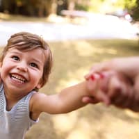 Mimik und eine ausgeprägte Fähigkeit zur Kommunikation mit der Umwelt zeichnen starke Kinder aus. Fröhliches Kind hält die Hände der Eltern.