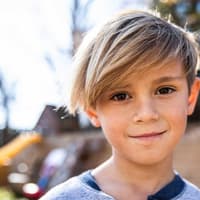 Jungs-Frisuren: Inspirationen für den Friseur-Besuch Blonder Junge mit längeren Haaren lächelt.