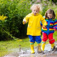 Tolle Pfützenspiele für Regentage gibt es hier. Kinder spielen in Pfützen.