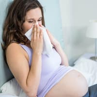 Eine Erkältung in der Schwangerschaft ist in der Regel nicht gefährlich, aber nervig! Schwangere Frau putzt sich die Nase.