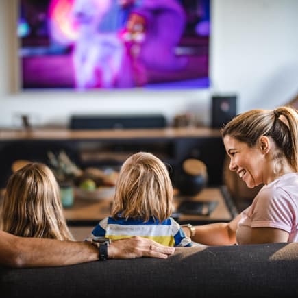 Mutter und Vater sitzen mit Sohn und Tochter auf dem Sofa vor dem Fernseher.