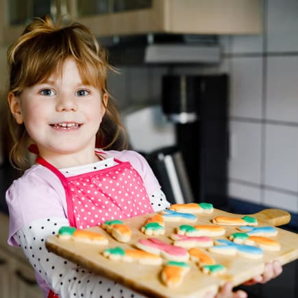 Osterkekse für Kinder sind schnell gemacht. Ein kleines Mädchen hält ein Küchenbrett mit Osterkeksen.
