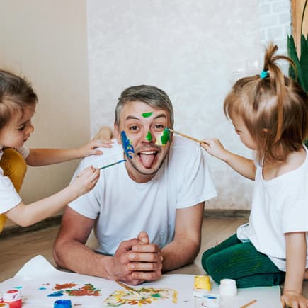 Ein männlicher Erzieher lässt sich in der Kita von zwei Kindern im Gesicht anmalen. Ein männlicher Erzieher lässt sich in der Kita von zwei Kindern im Gesicht anmalen.