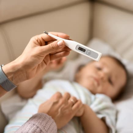 Fiebersaft oder Zäpfchen, was wirkt schneller? Eine Mutter hält das Fieberthermometer über ihrem Baby.