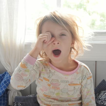 Gerade für Kinder ist die Zeitumstellung nicht immer leicht. Blondes Mädchen reibt sich am Morgen die Augen und gähnt