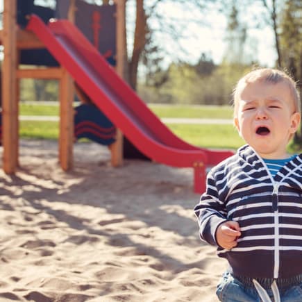 Kleiner Junge sitzt weinend vor einer Rutsche im Sand Kleiner Junge sitzt weinend vor einer Rutsche im Sand