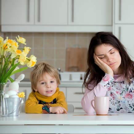 Wer einen kleinen Frühaufsteher zu Hause hat, braucht starken Kaffee. Mama sitzt müde am Tisch, Kind ist hellwach