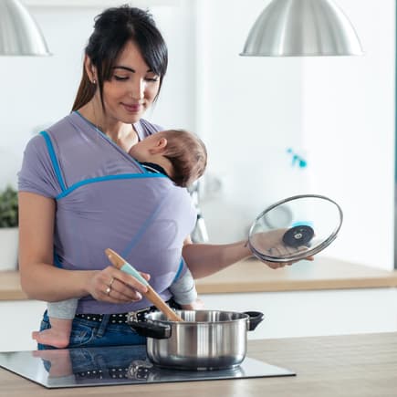 Mama mit Baby in Babytrage beim Kochen Mama mit Baby in Babytrage beim Kochen