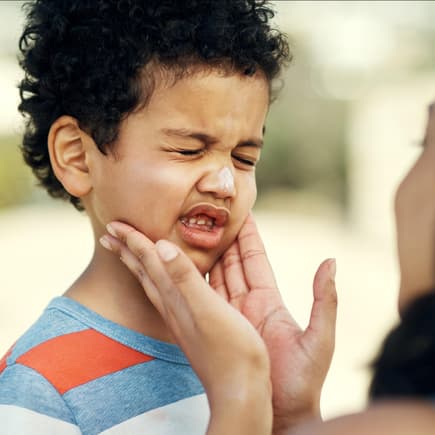 Sonnenschutz im Kindergarten: Wer cremt ein? Kleiner Junge wird mit Sonnencreme eingeschmiert.