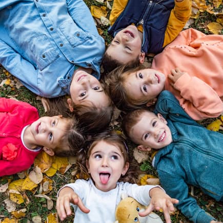 Kita-Kinder liegen im Herbstlaub und singen Herbstlieder im Kindergarten. Kita-Kinder liegen im Herbstlaub und singen Herbstlieder im Kindergarten.