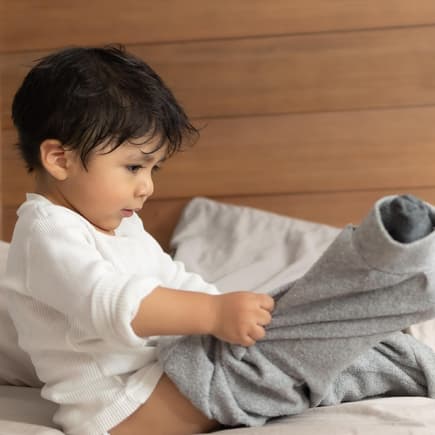 Unpraktische Kleidung für Kinder Ein Kind zieht sich selbst an.