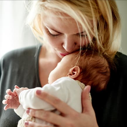 Frau küsst neugeborenes Baby auf die Stirn. Ist es wirklich so schlimm, ein Neugeborenes zu küssen?