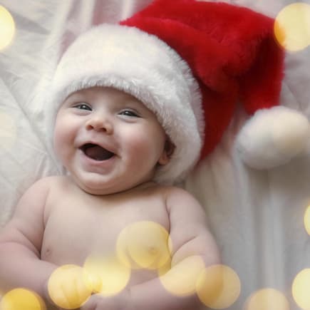 Weihnachtliche Babynamen sind einen besonders klangvoll. Lachendes Baby mit Weihnachtsmütze.