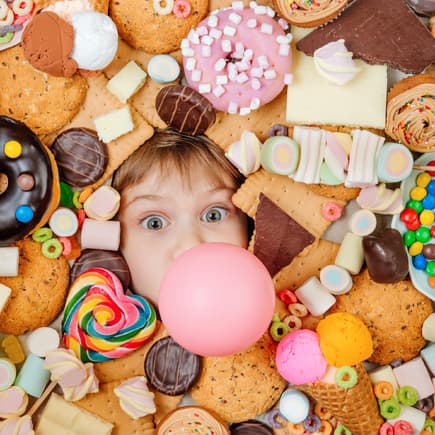 Zucker für Kinder ist sehr umstritten. Kleines Kind, das unter vielen süßen Speisen liegt.