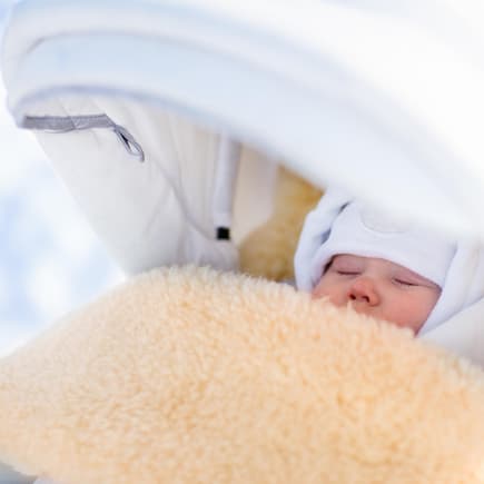 In Skandinavien lassen Eltern ihre Babys auch im Winter draußen schlafen. Baby schläft im Winter draußen im Kinderwagen.