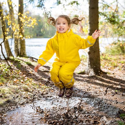 Draußen spielen beeinflusst die Entwicklung von Kindern positiv. Kind spielt draußen und springt in Pfütze