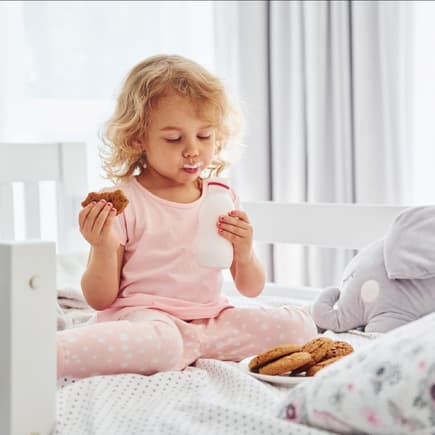 Nach dem Abendbrot noch Hunger ... Ein kleines Mädchen isst im Bett Kekse und trinkt Milch.