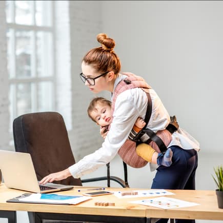 Berufstätige Mütter müssen sich nicht zwischen Kind oder Karriere entscheiden. Mutter am Schreibtisch mit Baby in der Trage.