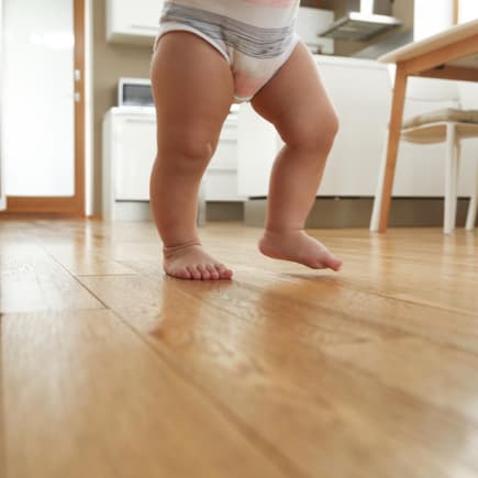 Lauflern-Trends können für Babys gefährlich sein. Babybeine beim Laufen in der Küche.