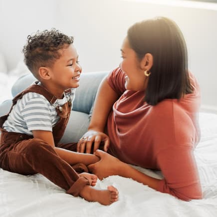 Kindern Grenzen setzen ist für Eltern oft nicht ganz leicht. Mutter und Sohn liegen auf dem Bett und unterhalten sich.