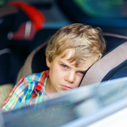 Darf man sein Kind alleine im Auto lassen? Dieses Frage stellen sich viele Eltern früher oder später. Ein kleiner Junge schaut aus dem offenen Autofenster.